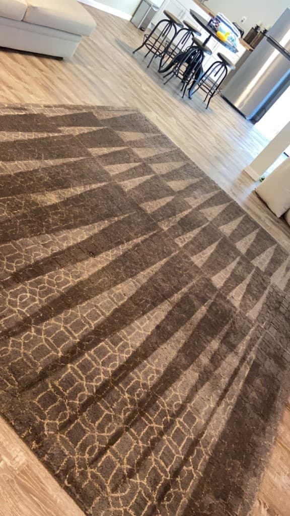 Large brown geometric area rug on a wood floor beside dining furniture