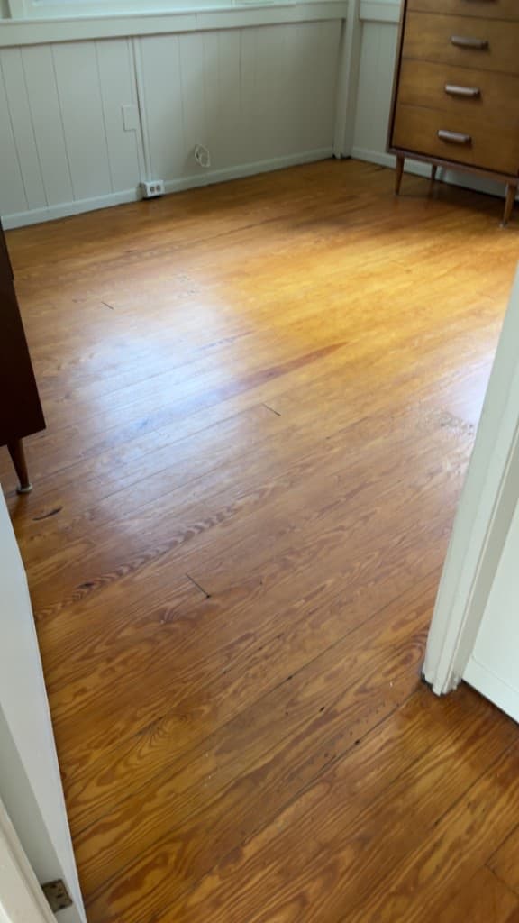 Warm wood plank flooring in a sparsely furnished room viewed through a doorway